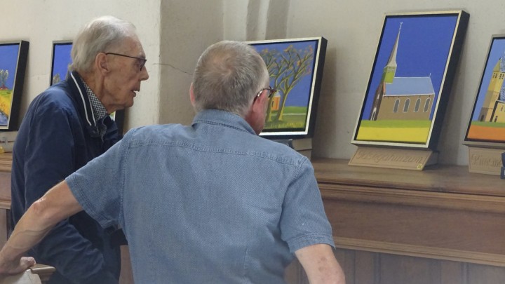 Douwe Bonnema (links) bekijkt met predikant Helmer le Cointre zijn schilderijen van kerken.
