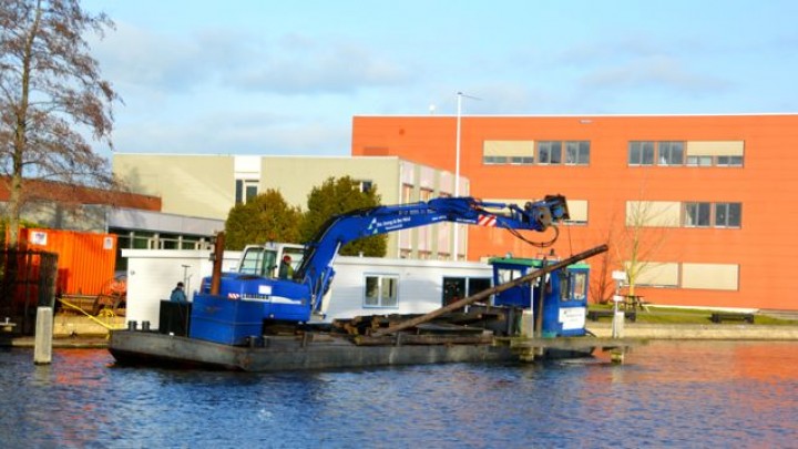 Een bouwbedrijf legt de woonboot aan de wal bij het kantoor van de FUMO, het voormalige gemeentekantoor.